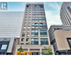 A tall building with a glass facade stands in front of other buildings.