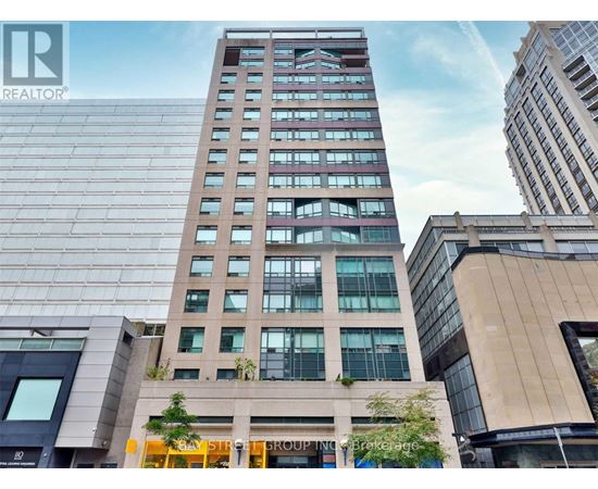 A tall building with a glass facade stands in front of other buildings.