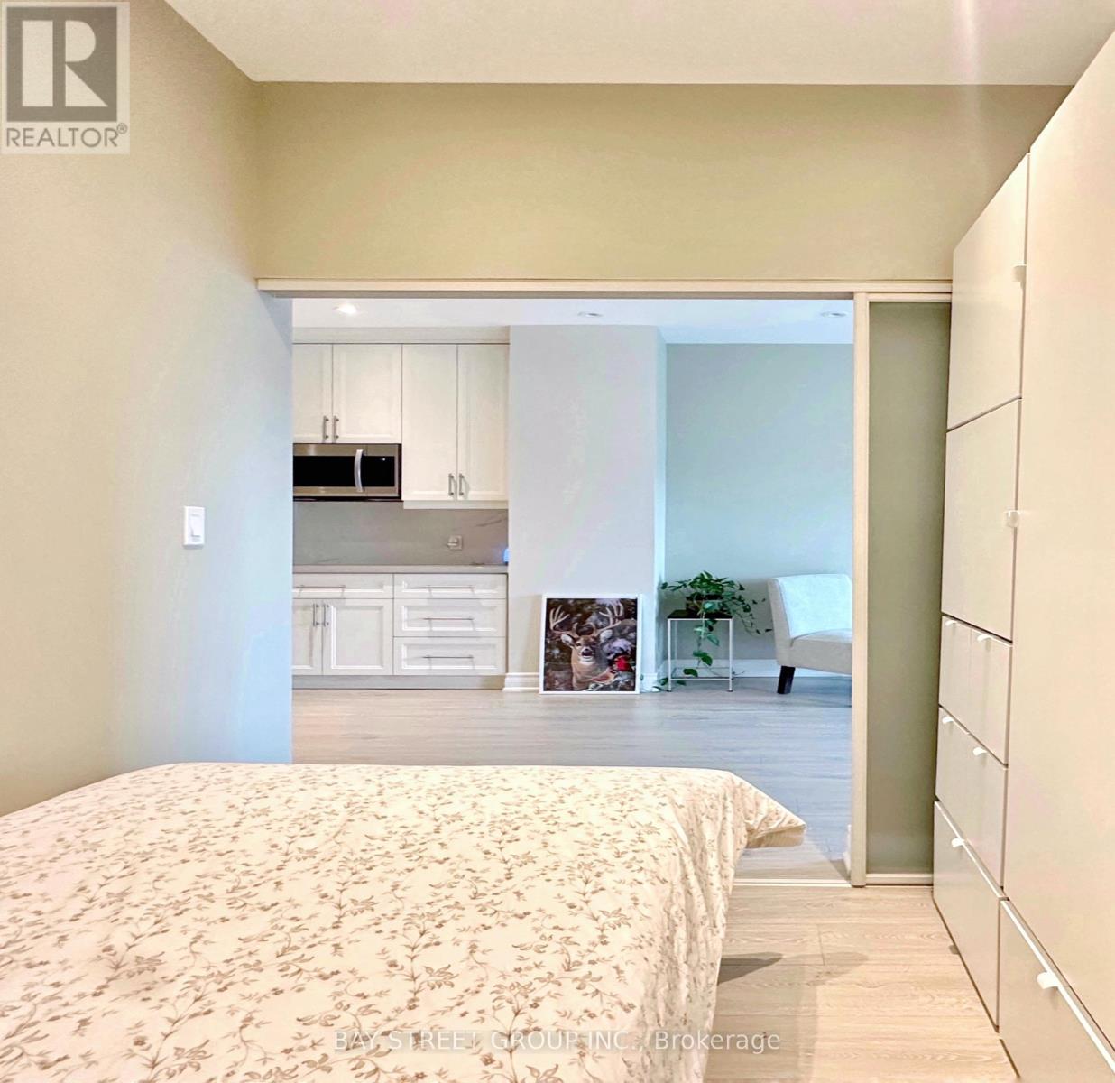 A bedroom with a large bed and a kitchen area in the background.