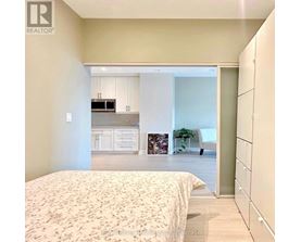 A bedroom with a large bed and a kitchen area in the background.