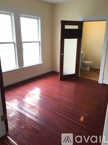 A room with a wooden floor and a door leading to a bathroom.