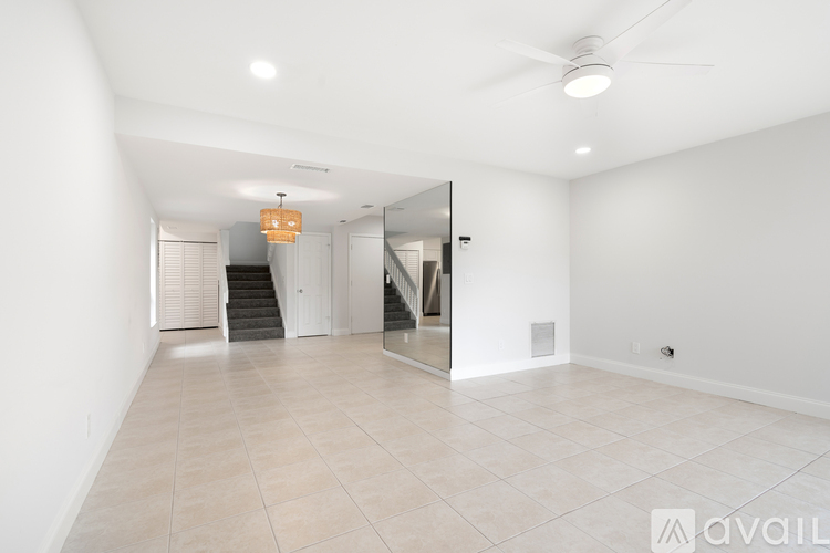 A spacious, empty room with a staircase and a ceiling fan.