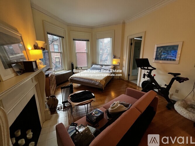 A living room with a fireplace and a bed in the background.