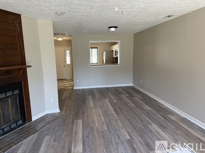A room with wooden flooring and a fireplace on the left side.