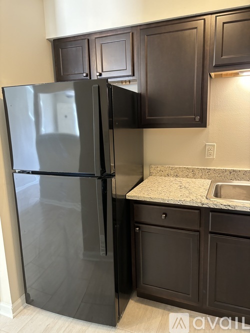A black refrigerator in a kitchen with brown cabinets.