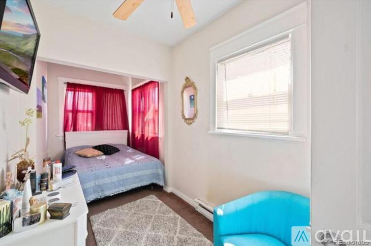A bedroom with a bed, a window with red curtains, and a ceiling fan.