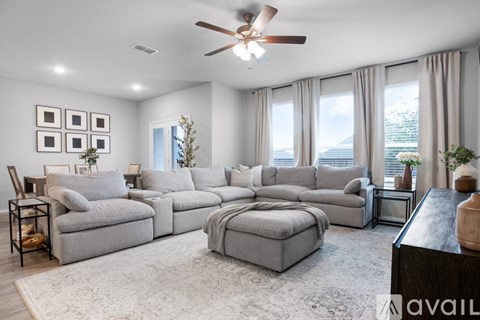 A spacious living room with a grey sofa set and a ceiling fan.