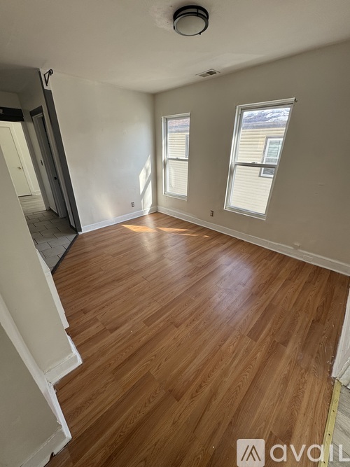 A room with wooden flooring and two windows.