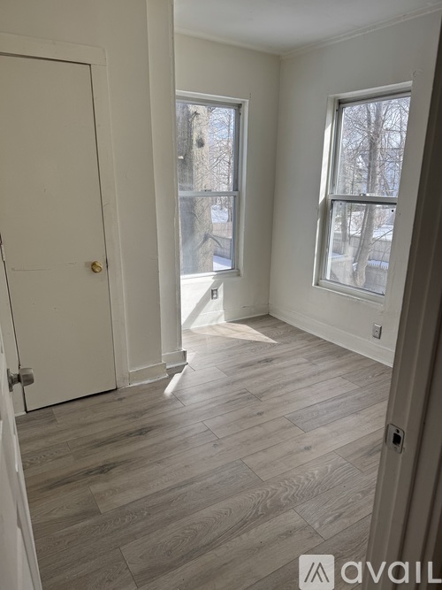 A room with a white door and two windows with wooden flooring.