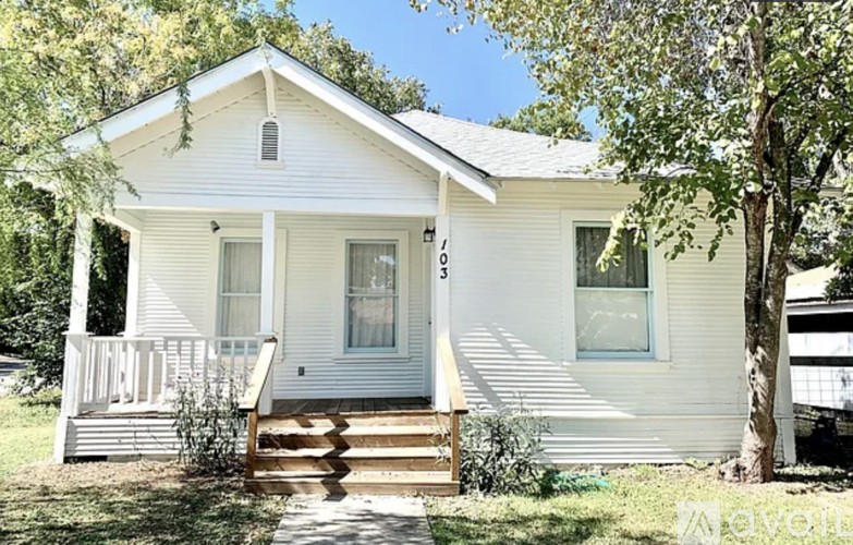 A white house with a porch and a tree in front.