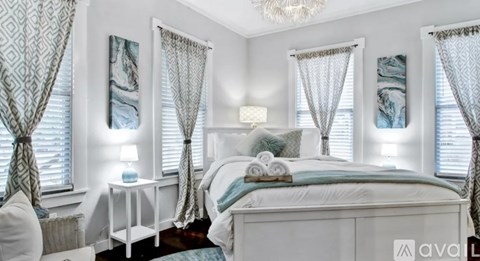A bedroom with a large bed, a nightstand with a lamp, and a chandelier.