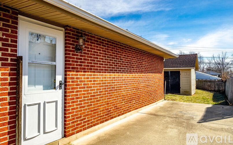 A red brick house with a white door and a small shed in the backyard.