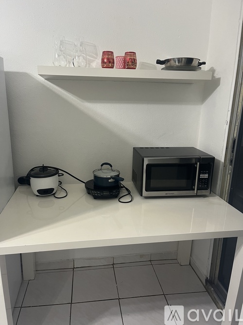 A white kitchen counter with a microwave, kettle, and pot on it.