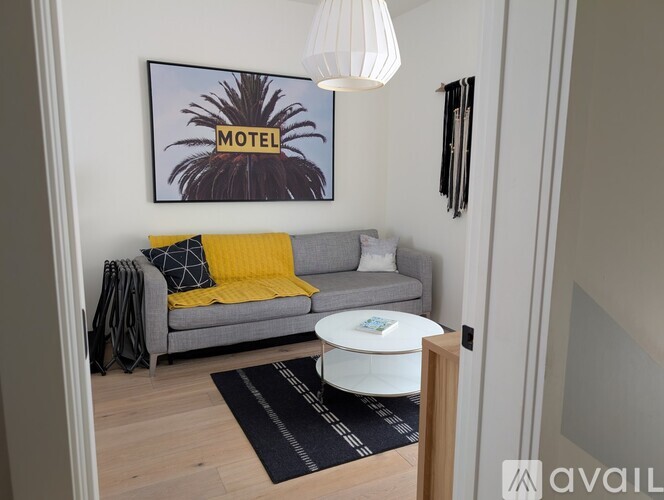A living room with a grey couch, a yellow throw, and a framed picture of a palm tree on the wall.