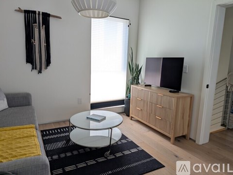 A living room with a grey couch, a glass table, a TV, and a plant.
