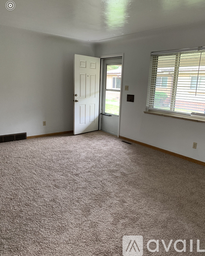 A room with a carpeted floor, a door, and a window with blinds.
