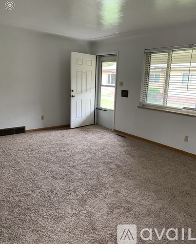 A room with a carpeted floor, a door, and a window with blinds.