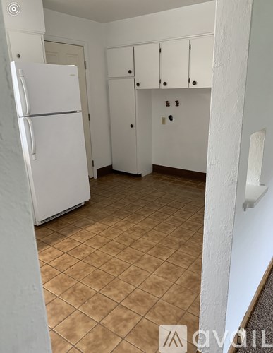A kitchen with a white fridge and brown tiled floor.