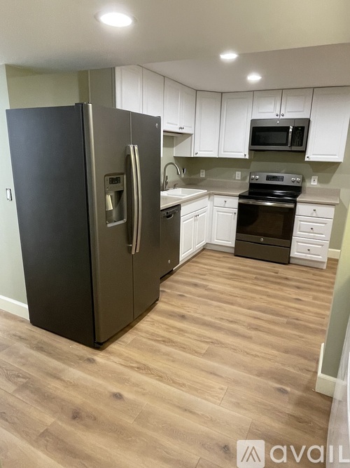 A black refrigerator stands in a kitchen with white cabinets and wooden floors.