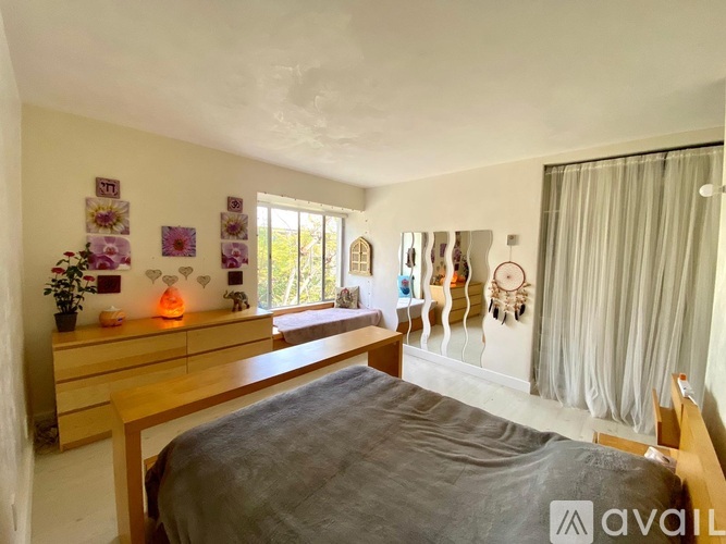 A bedroom with a bed, dresser, and a window with curtains.