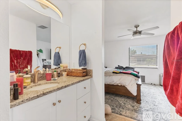 A bathroom with a mirror, sink, and a bedroom with a bed and a fan.