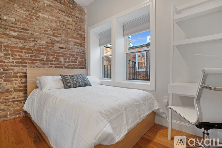 A bedroom with a white bed and a brick wall.