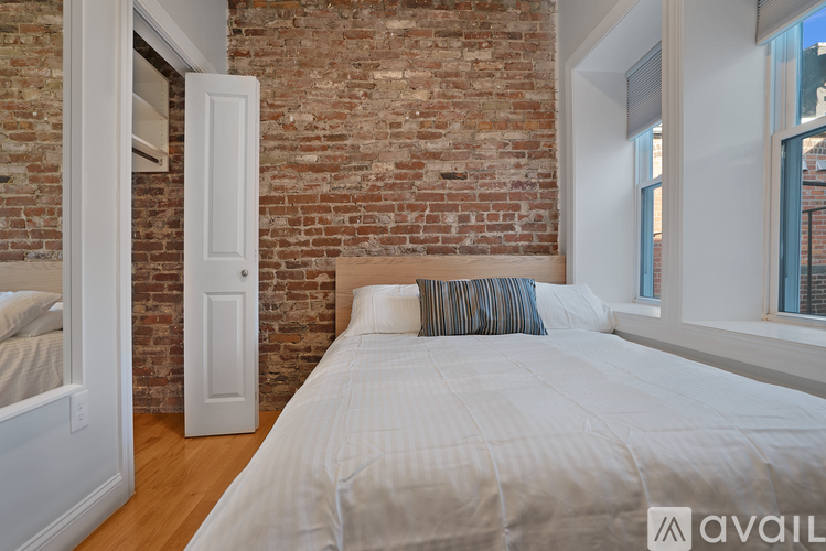 A bedroom with a brick wall and a bed with white bedding.