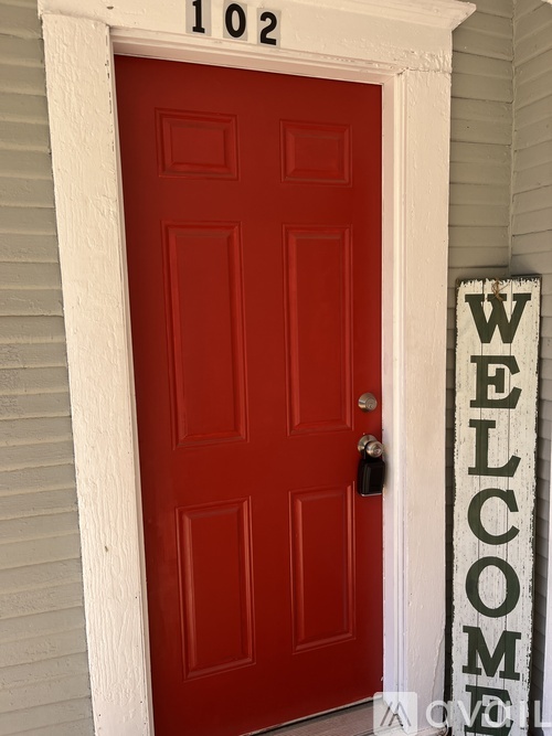 A red door with a white frame and a sign that says "Welcome".