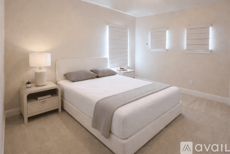 A bedroom with a large bed, a nightstand with a lamp, and a window with blinds.