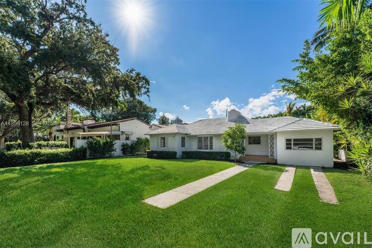 A white house with a green lawn and trees around it.