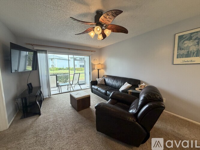 A living room with a black leather couch and a ceiling fan.