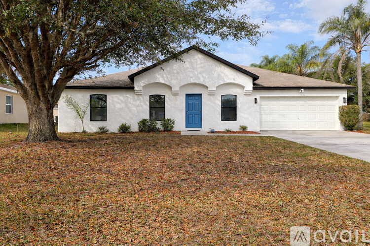 A white house with a blue door stands alone in a field of fallen leaves.