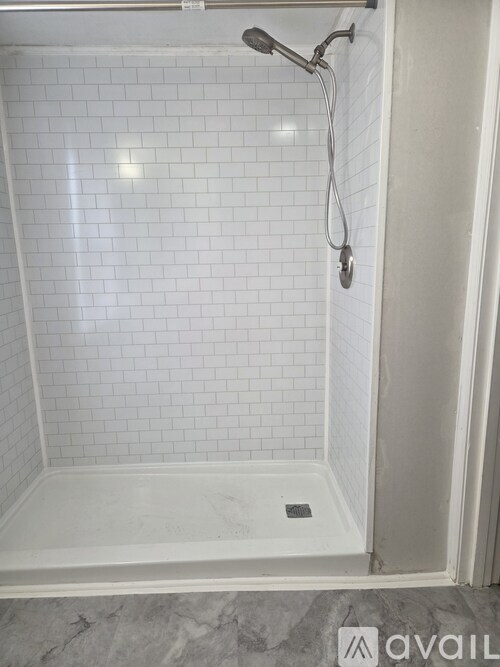 A white tiled shower with a shower head and a drain.