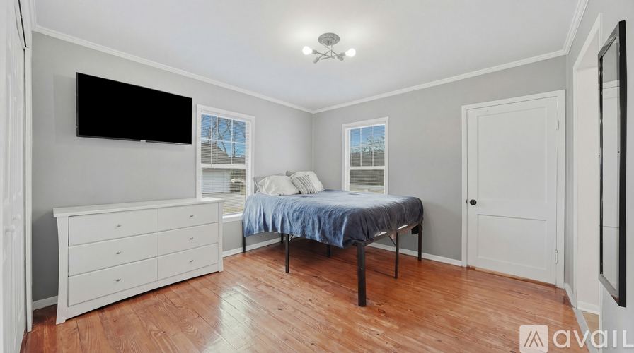 A bedroom with a bed, dresser, and a flat screen TV mounted on the wall.