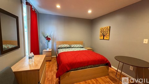 A bedroom with a red bedspread and a painting on the wall.