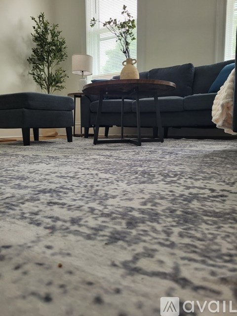 A living room with a grey sofa, a small table with a vase and a lamp, and a grey rug.