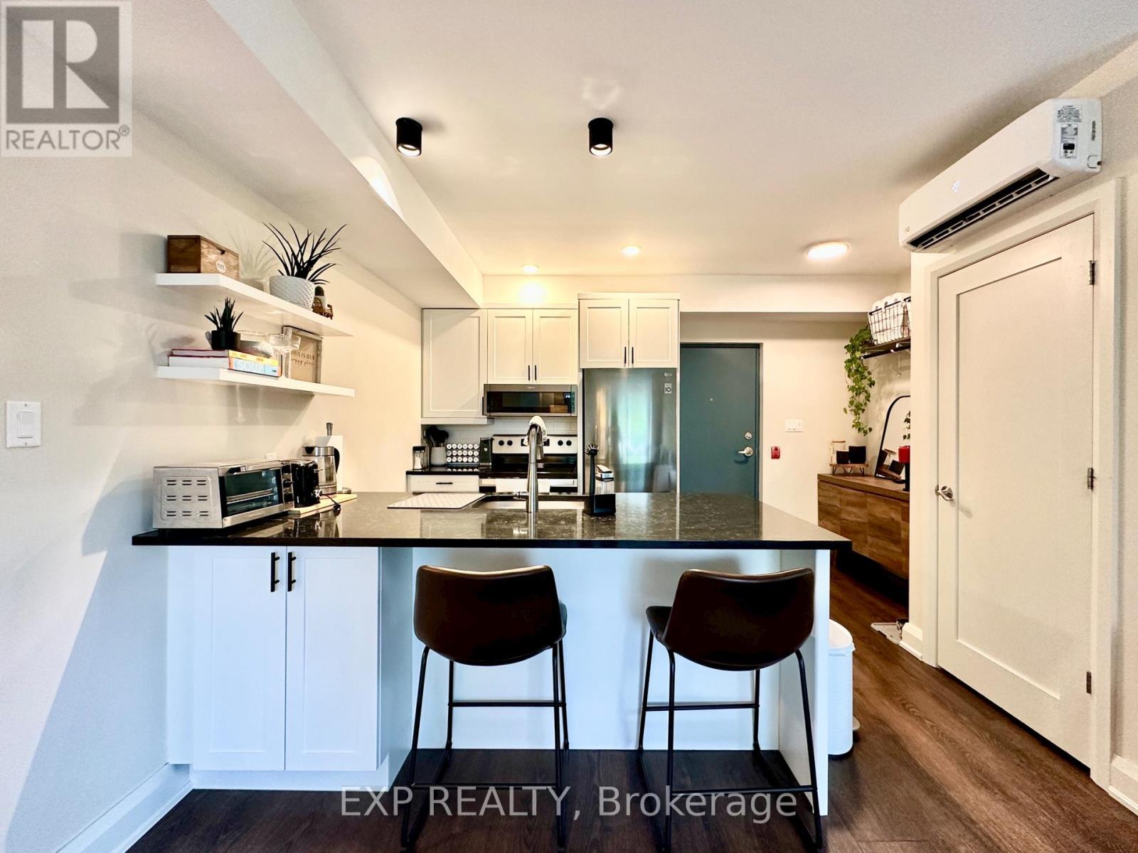 A kitchen with white cabinets and a black countertop with two chairs.