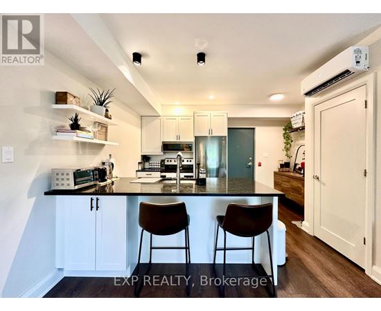 A kitchen with white cabinets and a black countertop with two chairs.