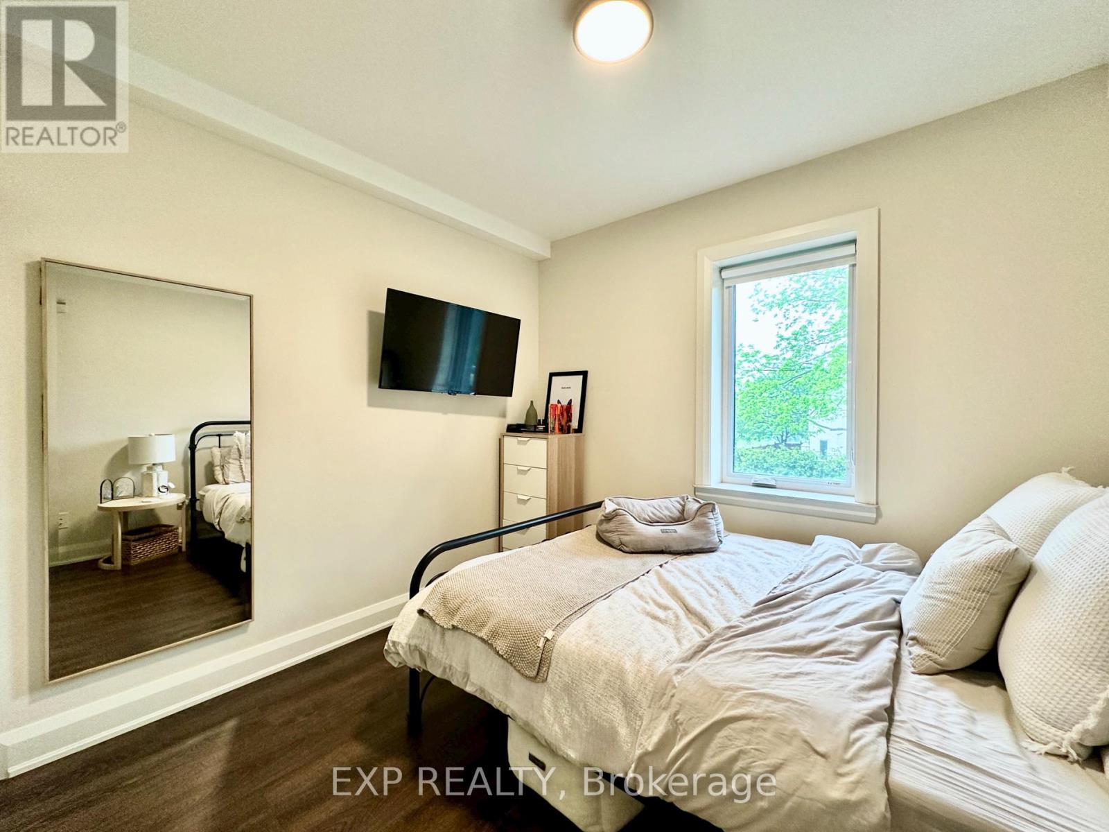 A bedroom with a bed, dresser, mirror, and window.