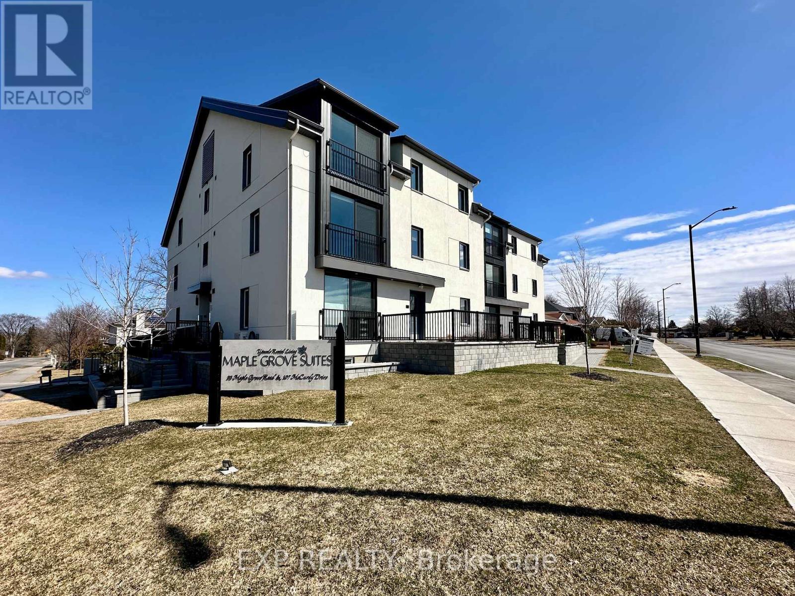 Maple Grove Suites is a modern apartment complex with a well-maintained lawn and a clear blue sky overhead.