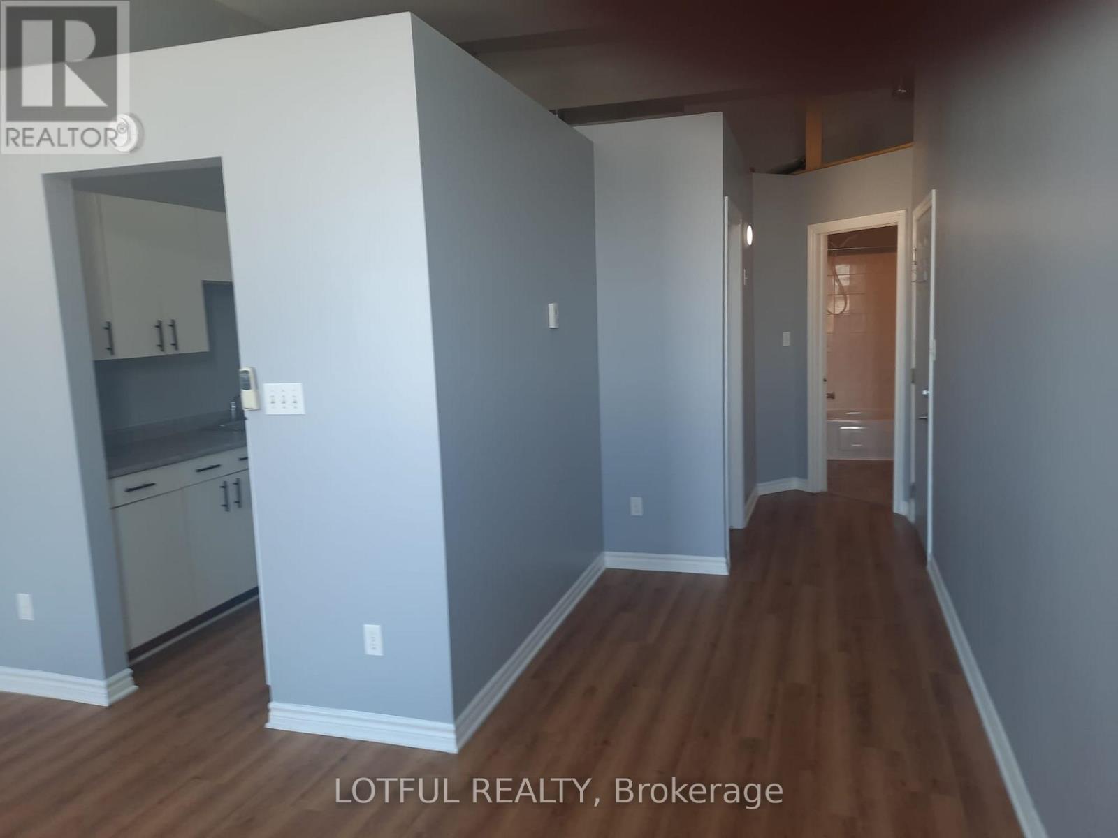 A room with wooden floors and a kitchen area with white appliances.
