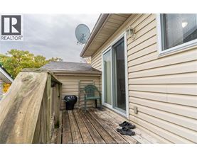 A wooden deck with a pair of shoes and a green chair is in front of a house.