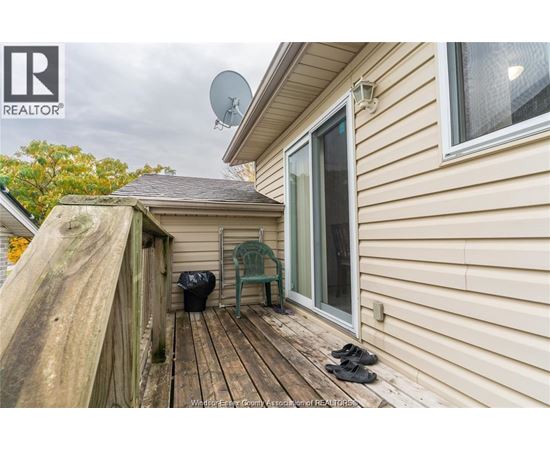 A wooden deck with a pair of shoes and a green chair is in front of a house.