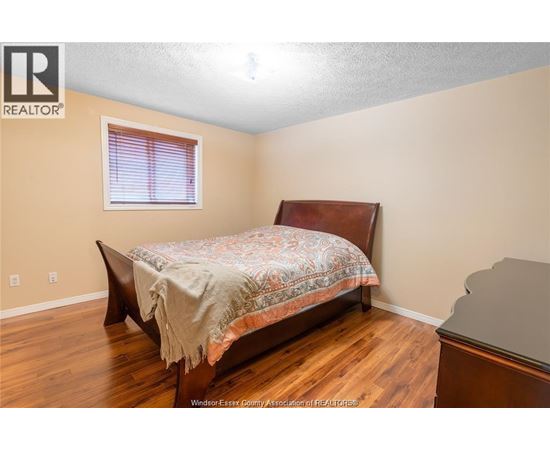A bedroom with a bed, wooden floors, and a window with blinds.