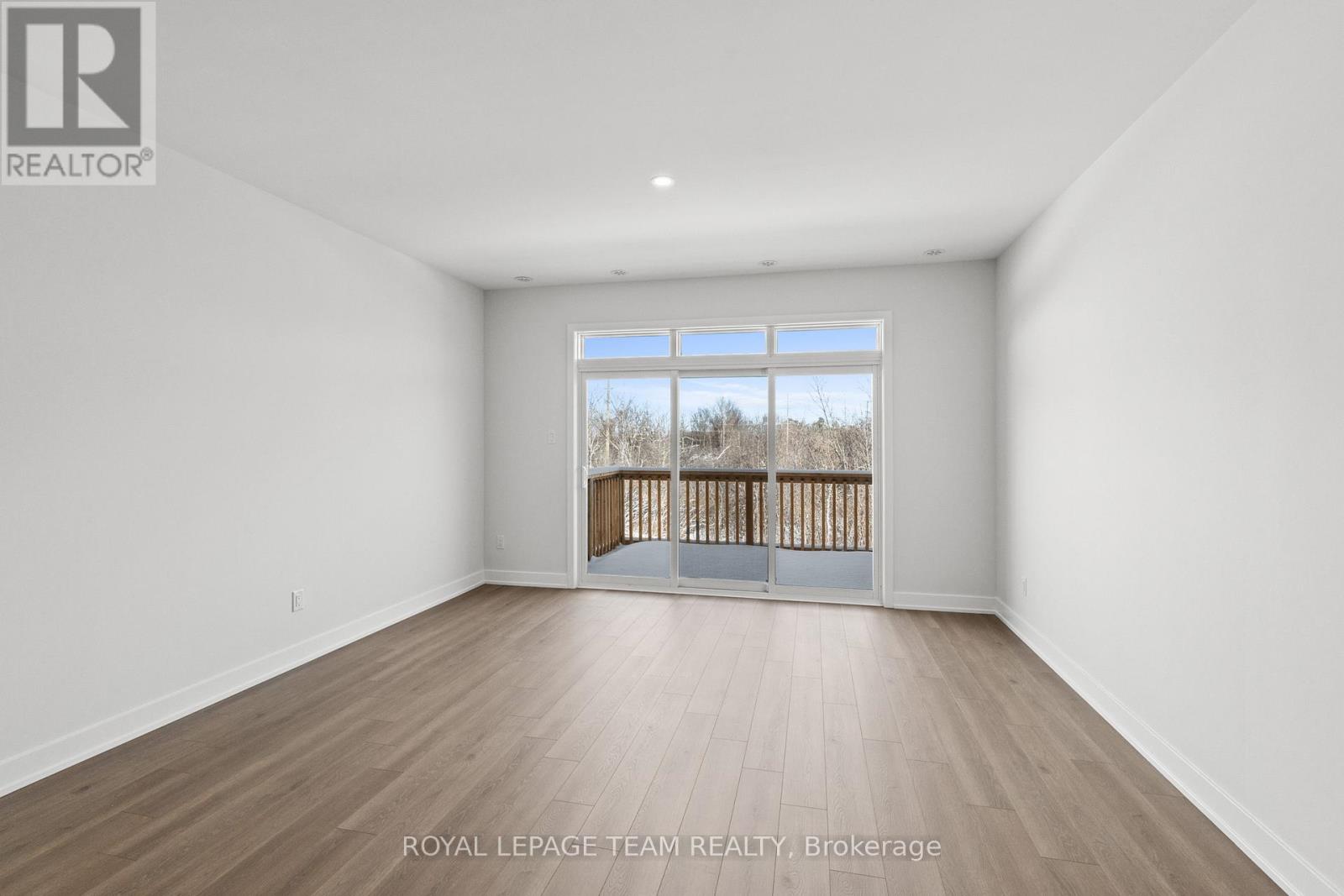 A spacious room with wooden flooring and a large window overlooking a wooden fence.