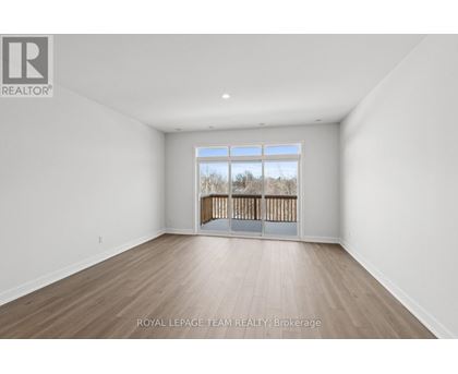 A spacious room with wooden flooring and a large window overlooking a wooden fence.