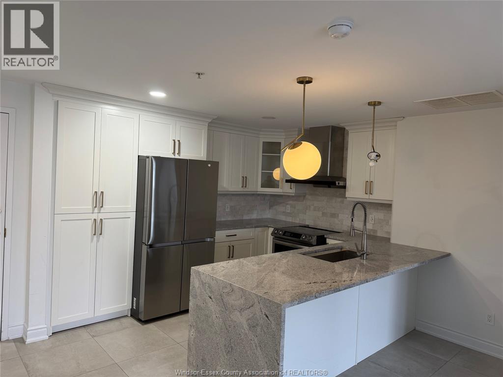 A kitchen with a refrigerator, cabinets, and a marble countertop.