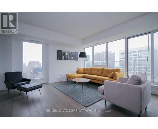 A living room with a yellow couch and a black chair.