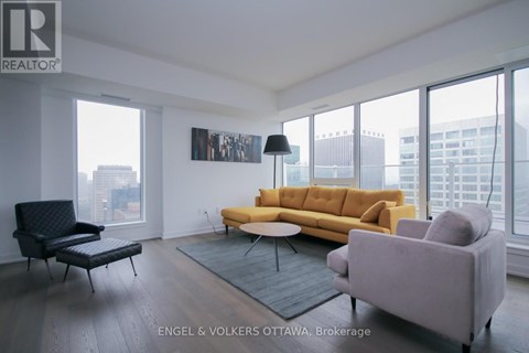 A living room with a yellow couch and a black chair.