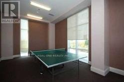 A glass table is in the middle of a room with a Realty logo on the wall.